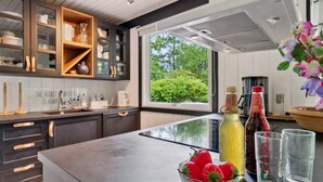 Una cucina moderna con mobili scuri, un'isola grande e vista sul verde circostante.