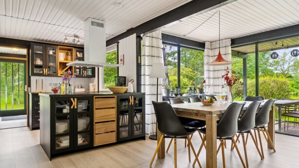 Una cucina moderna con isola centrale, pensili neri e zona pranzo con tavolo e sedie in legno.