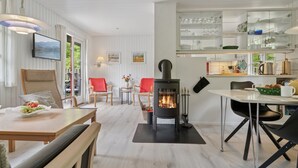 En hyggelig stue med pejs, spiseplads og et køkken med glaskabinetter.