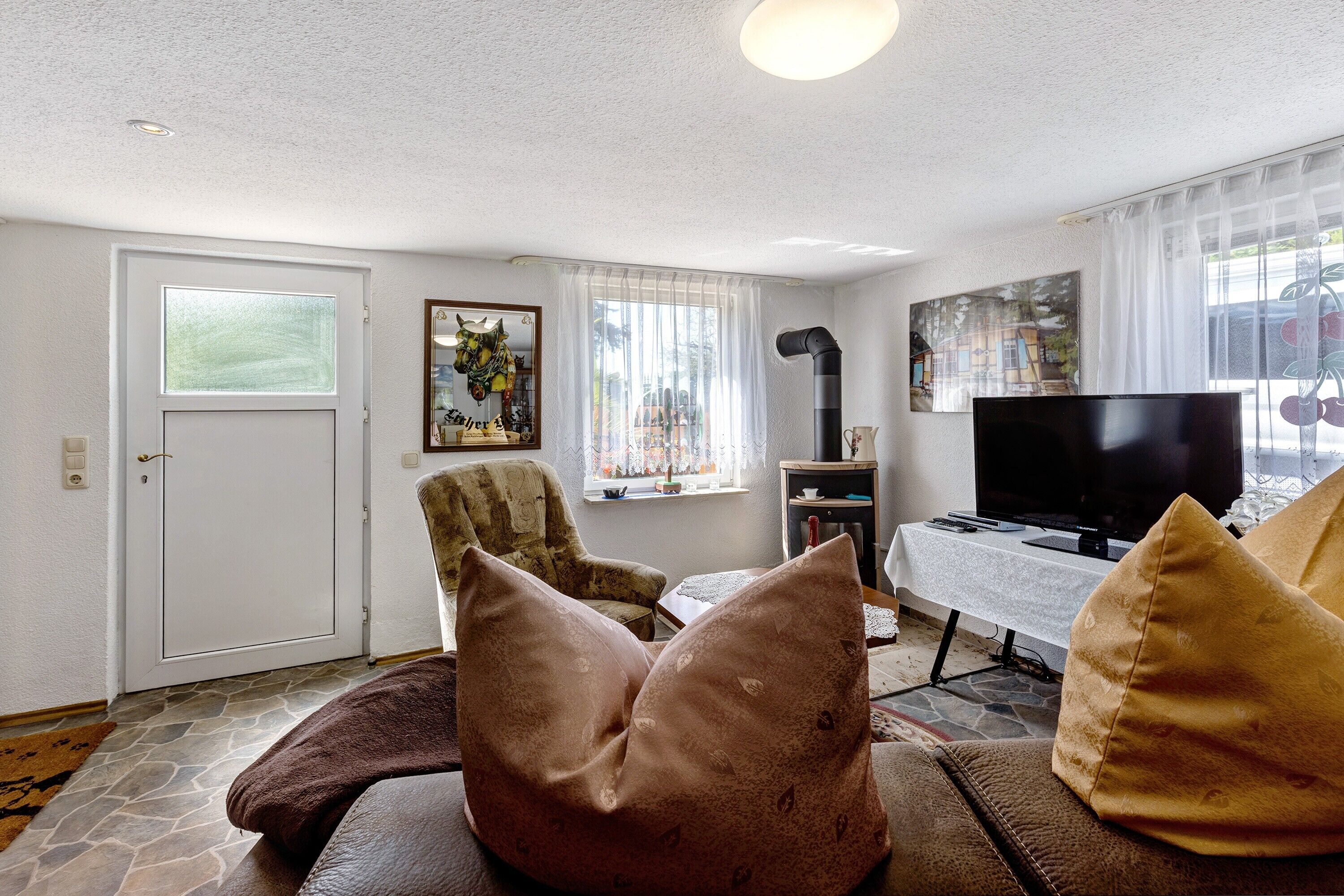 Una sala de estar con un sofá, un televisor, una ventana con cortinas, una puerta y un cuadro en la pared.