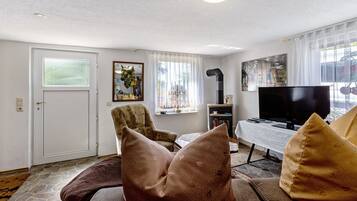 Una sala de estar con un sofá, un televisor, una ventana con cortinas, una puerta y un cuadro en la pared.