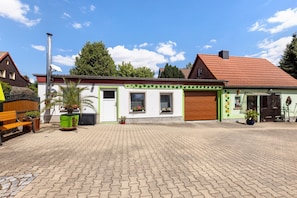 En bygning med en grøn og hvid facade, røde tegltage og en belagt gårdsplads med plantekrukker.