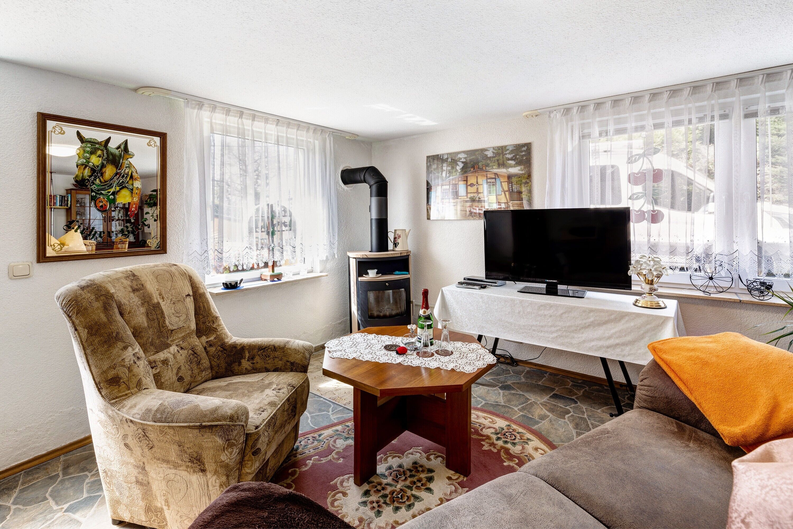 Een woonkamer met een bank, fauteuil, televisie, open haard en een tafel met een kantoneel.