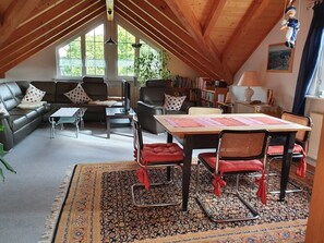 A cozy living room with a high ceiling, a sofa set, a coffee table, a dining table with chairs, and a bookshelf.