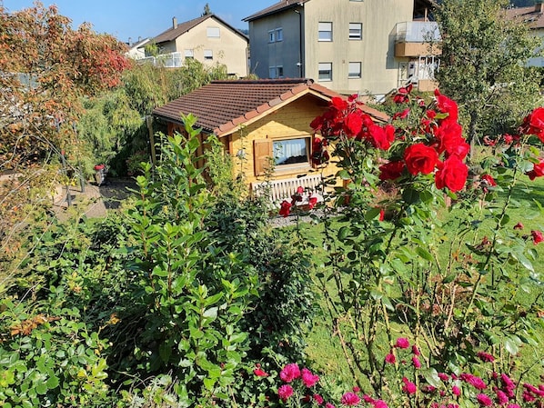 A wooden house with a sloped roof surrounded by lush greenery and flowering plants.
