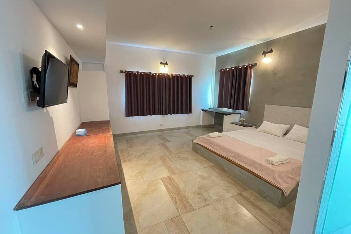 A modern hotel room with a bed, bedside table, TV, and a desk area.