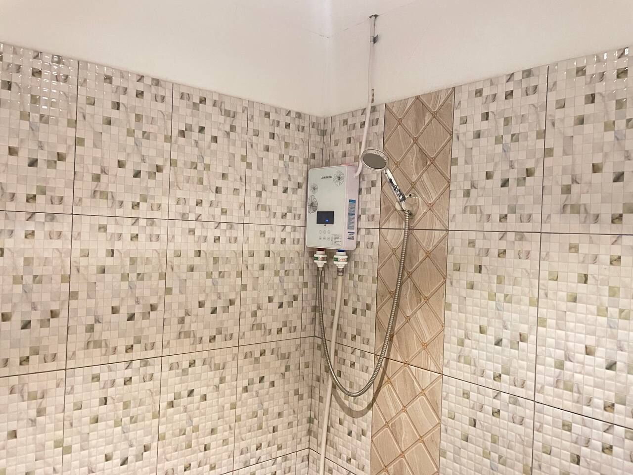 Zona de bany amb parets de mosaic i plat de dutxa manual.
