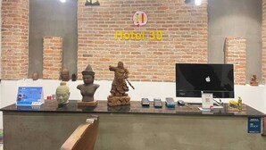 A reception desk with a brick wall background, a sign reading "Hotel 30", and various statues and electronic devices. - Hotel 30 (Phnom Penh)
