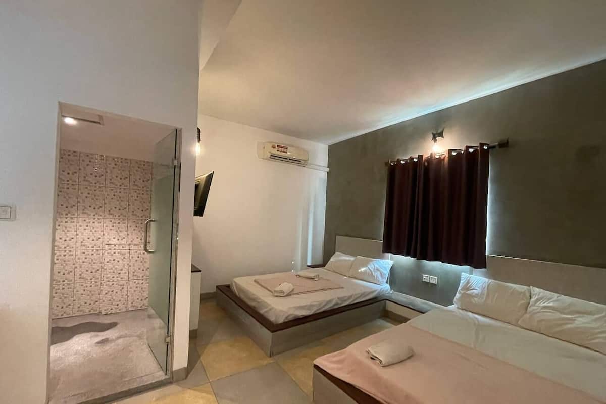 A modern hotel room with a glass shower enclosure, a bed with a headboard, and a bedside table.