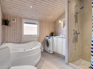 A bathroom with a bathtub, a washing machine, a shower, and a window.