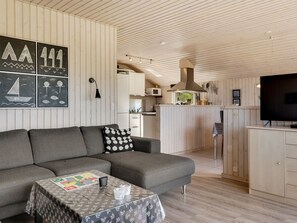 Un intérieur moderne comprenant un canapé, une petite table, un coin cuisine et un téléviseur.
