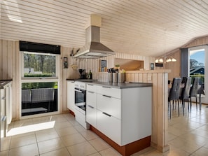 A modern kitchen with a central island, built-in oven, and a large window overlooking a garden.