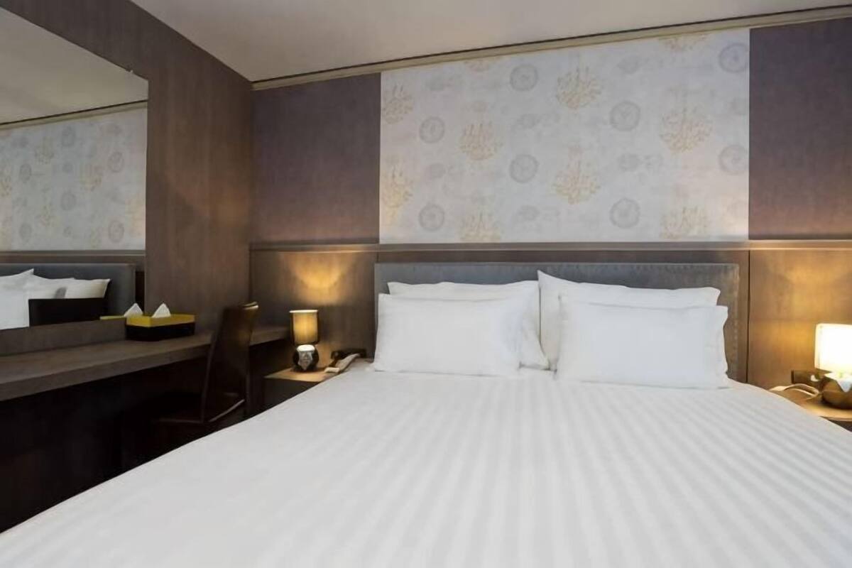 A hotel room with a large bed, bedside tables, a mirror, and a wall with patterned wallpaper.