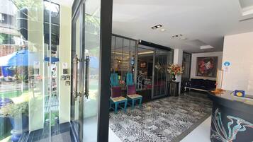 A modern hotel lobby with a glass door entrance, a patterned rug, and a blue chair.