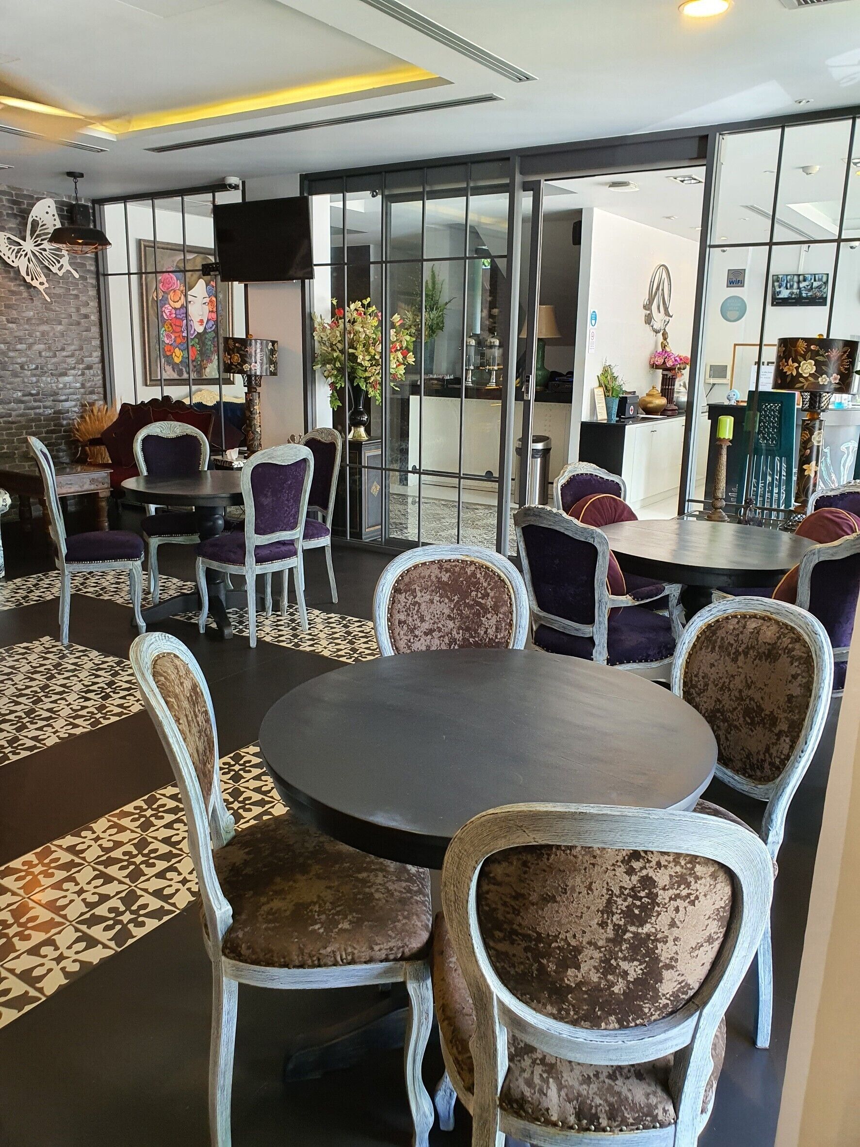 Un espace repas moderne avec des tables rondes et des chaises rembourrées, un papillon décoratif sur le mur et une grande fenêtre donnant sur l’extérieur.