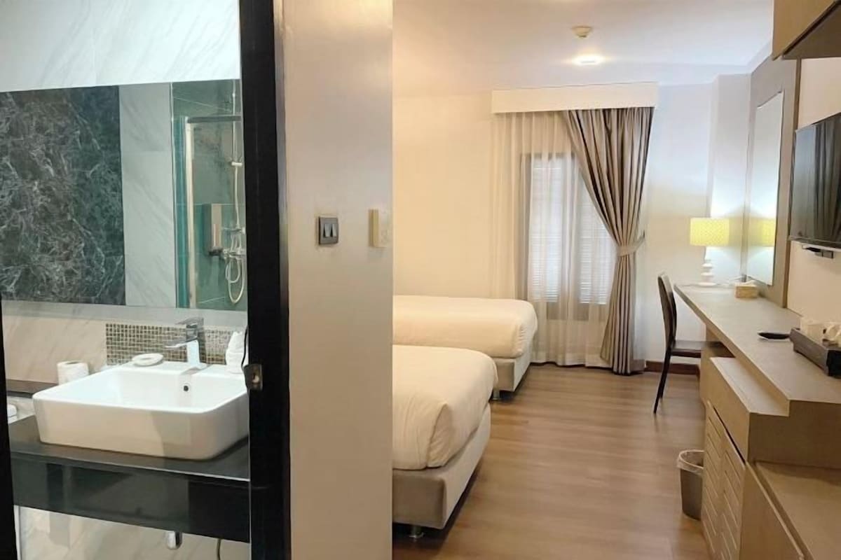 A hotel room with a bathroom, a bed, a desk, and a TV.