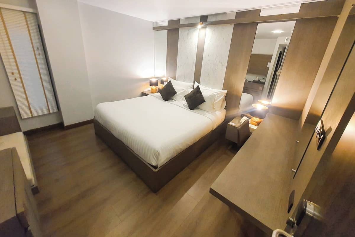 A modern hotel room with a large bed, bedside lamps, a wooden headboard, and a small bedside table.