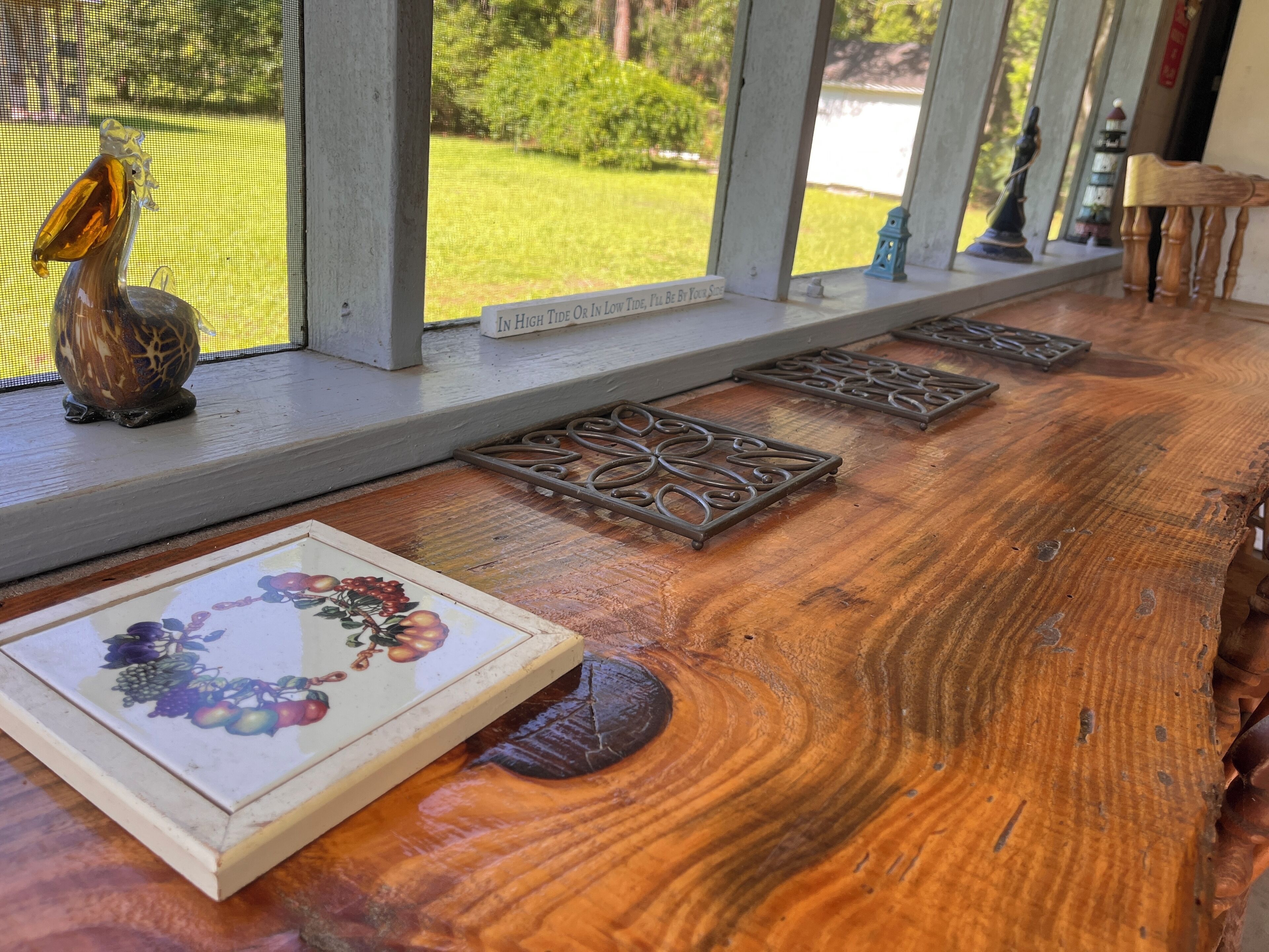 Une table en bois agrémentée de plateaux en métal décoratifs, une assiette en céramique ornée de motifs de fruits et une vue sur un jardin par la fenêtre.