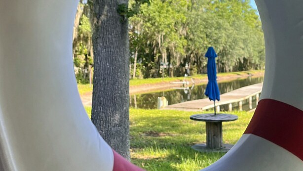 A lifebuoy with a view of a park, including a pond and a blue umbrella.