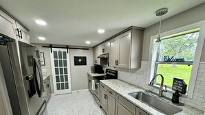 A modern kitchen with white cabinets, a stainless steel refrigerator, a microwave, and a sink.