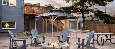 Eine Terrasse mit Adirondack-Stühlen, einem Feuerkorb und einer Holzpergola.