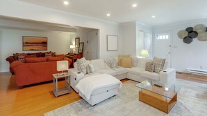 Een moderne woonkamer met een hoekbank, een glazen salontafel en een witte fauteuil.