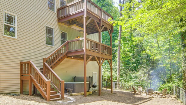Ein zweistöckiges Haus mit einer Holzterrasse und einer Sitzgelegenheit im Freien.