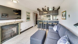 A modern kitchen with a bar area, a grey sofa, and a fireplace. - Walk to Angel Fire Lifts! Mountain-View Condo (Angel Fire)