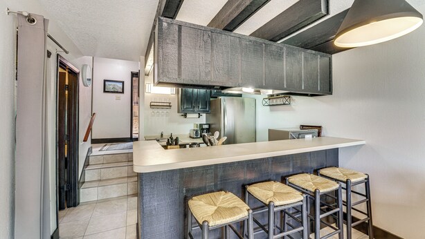 A modern kitchen with a bar area, featuring a large island with bar stools, a built-in oven, and a hanging light fixture. - Walk to Angel Fire Lifts! Mountain-View Condo (Angel Fire)