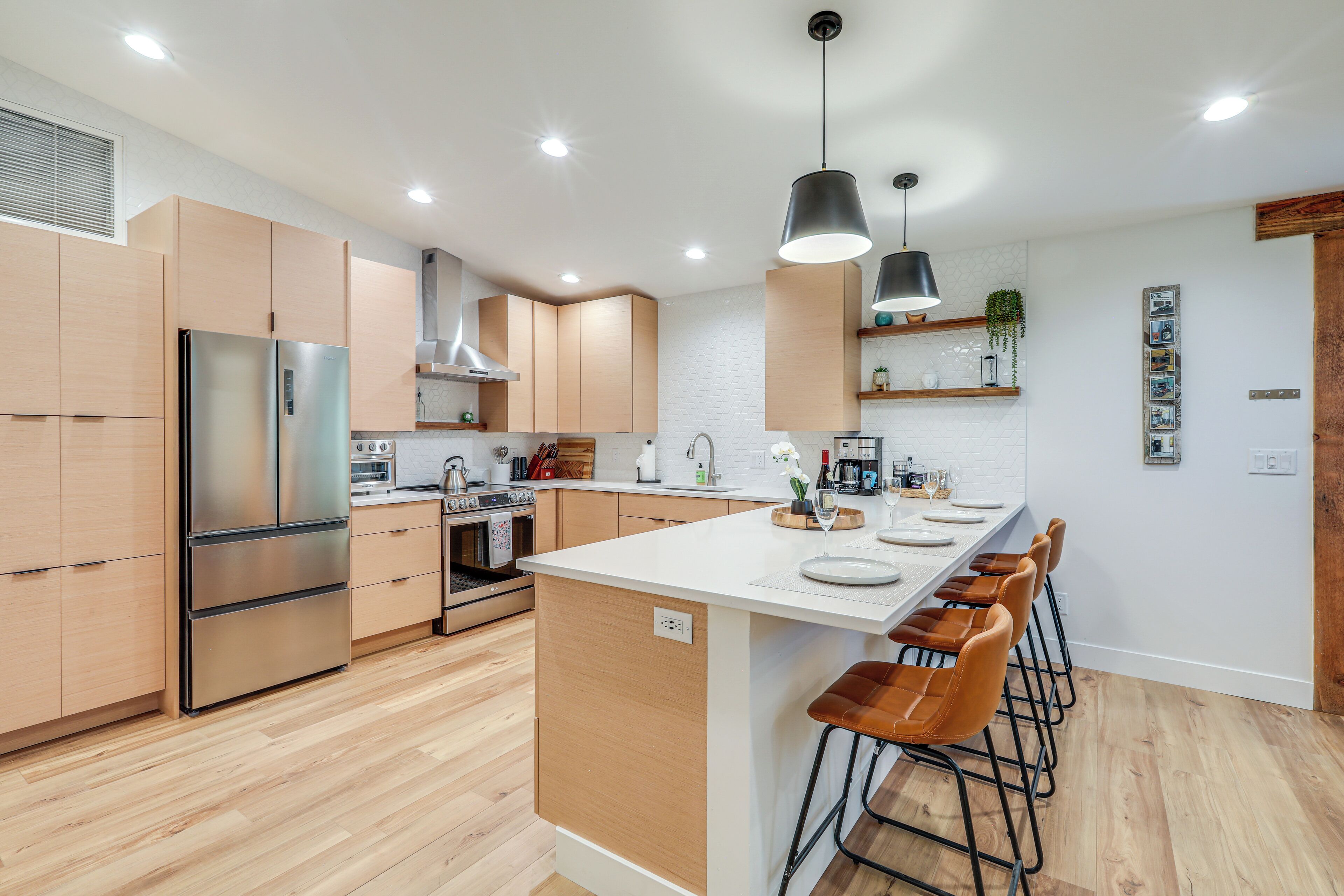 A modern kitchen with wooden cabinets, a stainless steel refrigerator, a central island with bar stools, and pendant lighting.