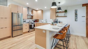 Una cucina moderna con mobili in legno, un frigorifero in acciaio inossidabile, un'isola centrale con sgabelli da bar e illuminazione a sospensione.