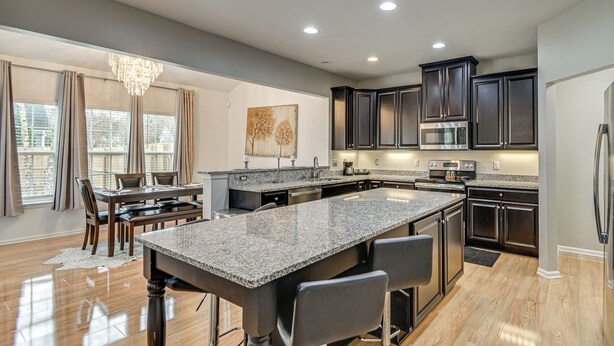 A modern kitchen with dark cabinets, granite countertops, and a central island with bar stools. - Fenced Yard & Patio! 2,400-Sq-Ft Chesapeake Home (Chesapeake)