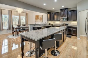 A modern kitchen with dark cabinets, granite countertops, and a central island with bar stools. - Fenced Yard & Patio! 2,400-Sq-Ft Chesapeake Home (Chesapeake)