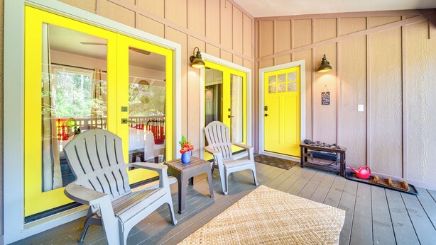 Eine Veranda mit zwei Adirondack-Stühlen, einem kleinen Tisch und einem Teppich.