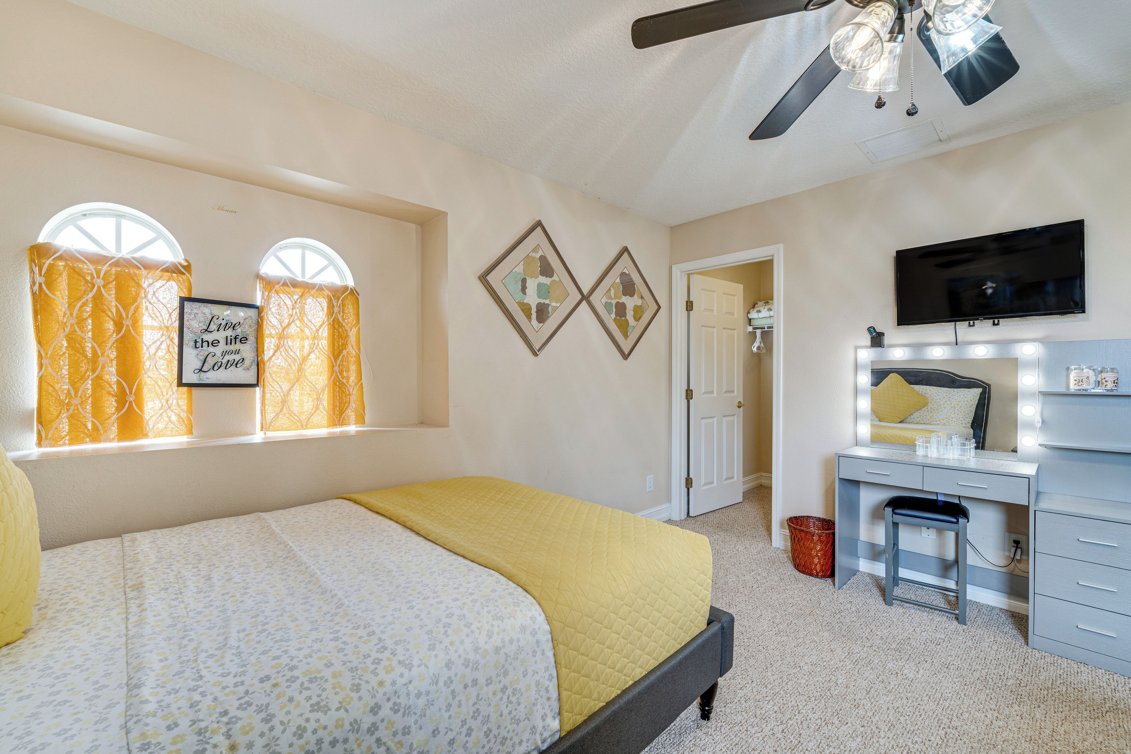 A bedroom with a bed, a vanity with a mirror, and a ceiling fan.