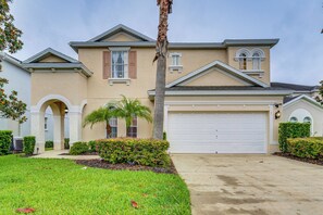 A two-story house with a beige exterior, a white garage door, and a well-maintained lawn. - 14 Mi to Disney: Spacious Home w/ Pool & Lanai! (Davenport)