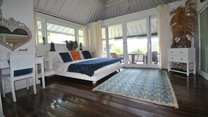 A bedroom with a bed, a desk, a chair, a large window, and a decorative plant.