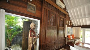 A room with a wooden cabinet, a statue, a sofa, and a view of greenery outside.