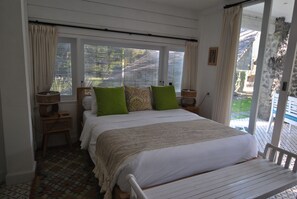 Un dormitorio con cama, ventana con cortinas, mesita de noche y una silla.