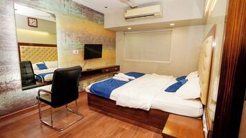 Une chambre d’hôtel moderne avec un plancher en bois, un lit avec une literie blanche et bleue, une chaise noire, un téléviseur à écran plat, un ventilateur de plafond et un appareil de climatisation.