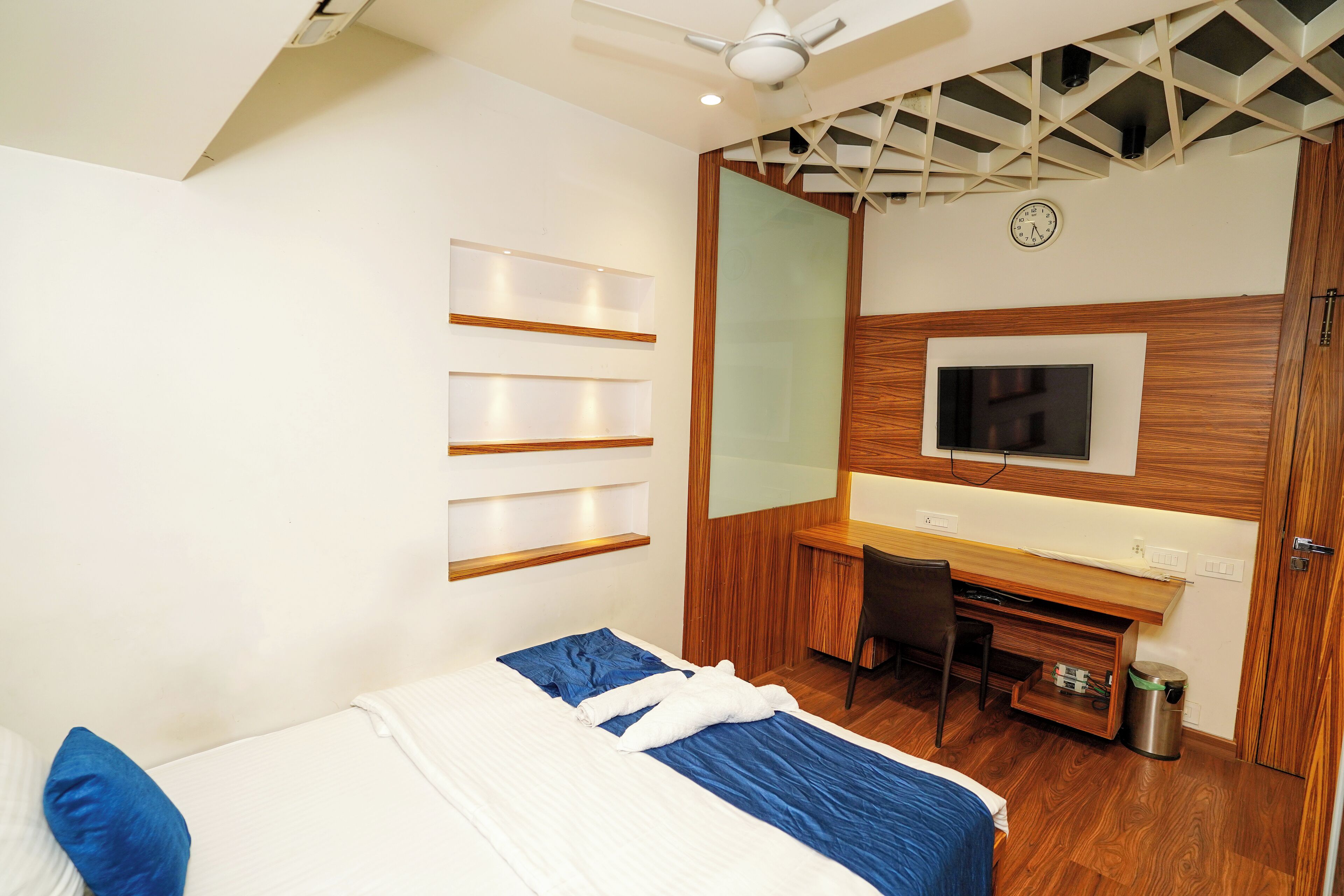 Een moderne hotelkamer met een bed, een bureau, een stoel, een televisie en een plafondventilator.