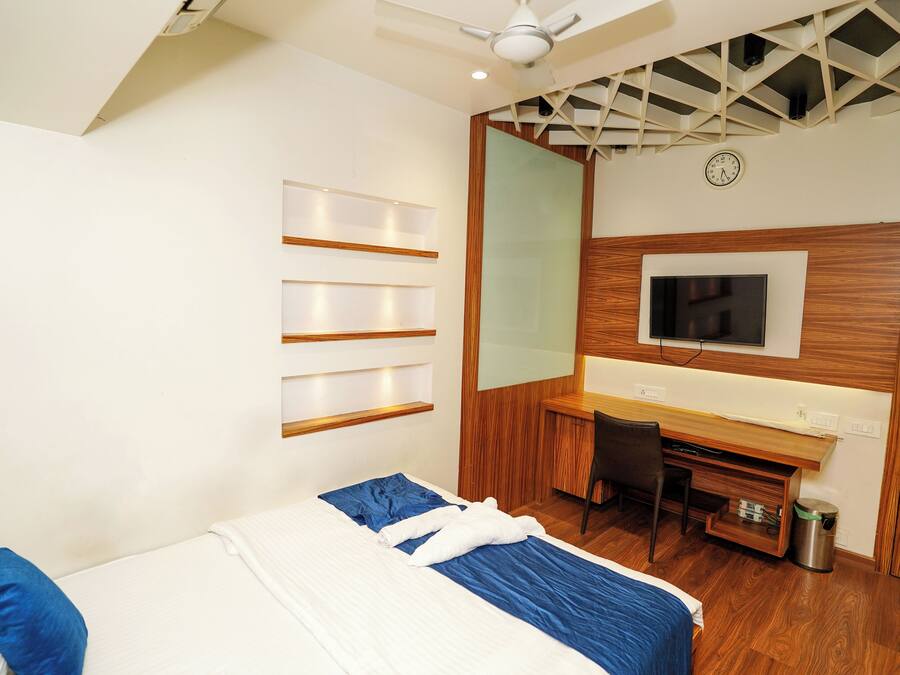 Een moderne hotelkamer met een bed, een bureau, een stoel, een televisie en een plafondventilator.