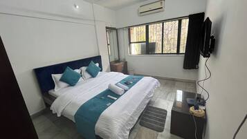 A hotel room with a bed, a ceiling fan, an air conditioning unit, a TV, and a window with curtains.