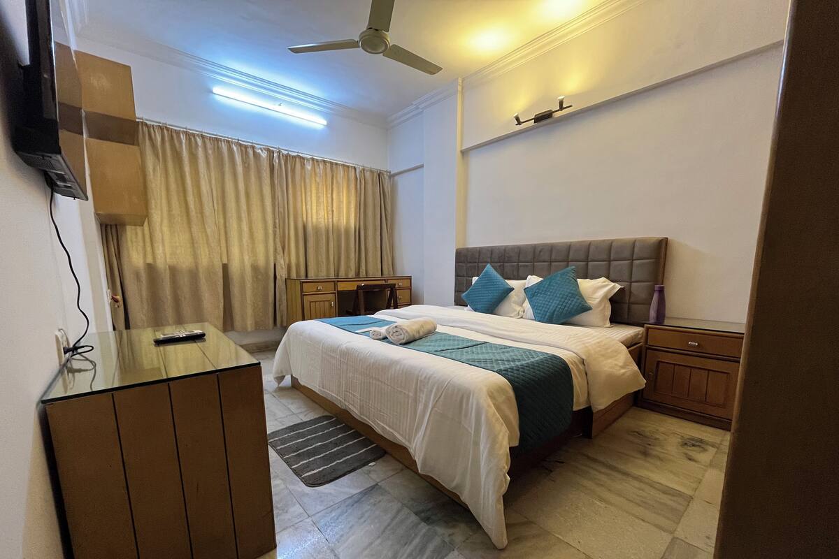 A hotel room with a bed, a desk, a chair, a TV, and a ceiling fan.