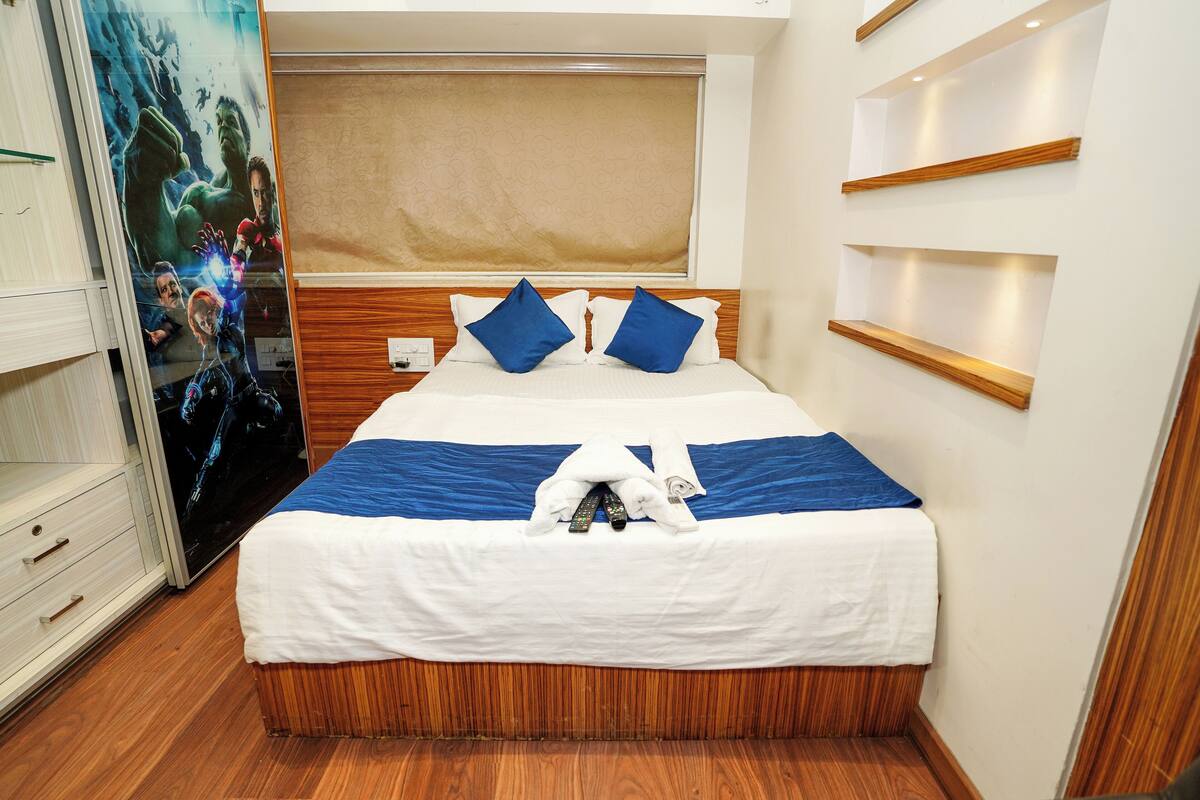 A neatly made bed with blue and white bedding, a wooden headboard, and a wall-mounted shelf.