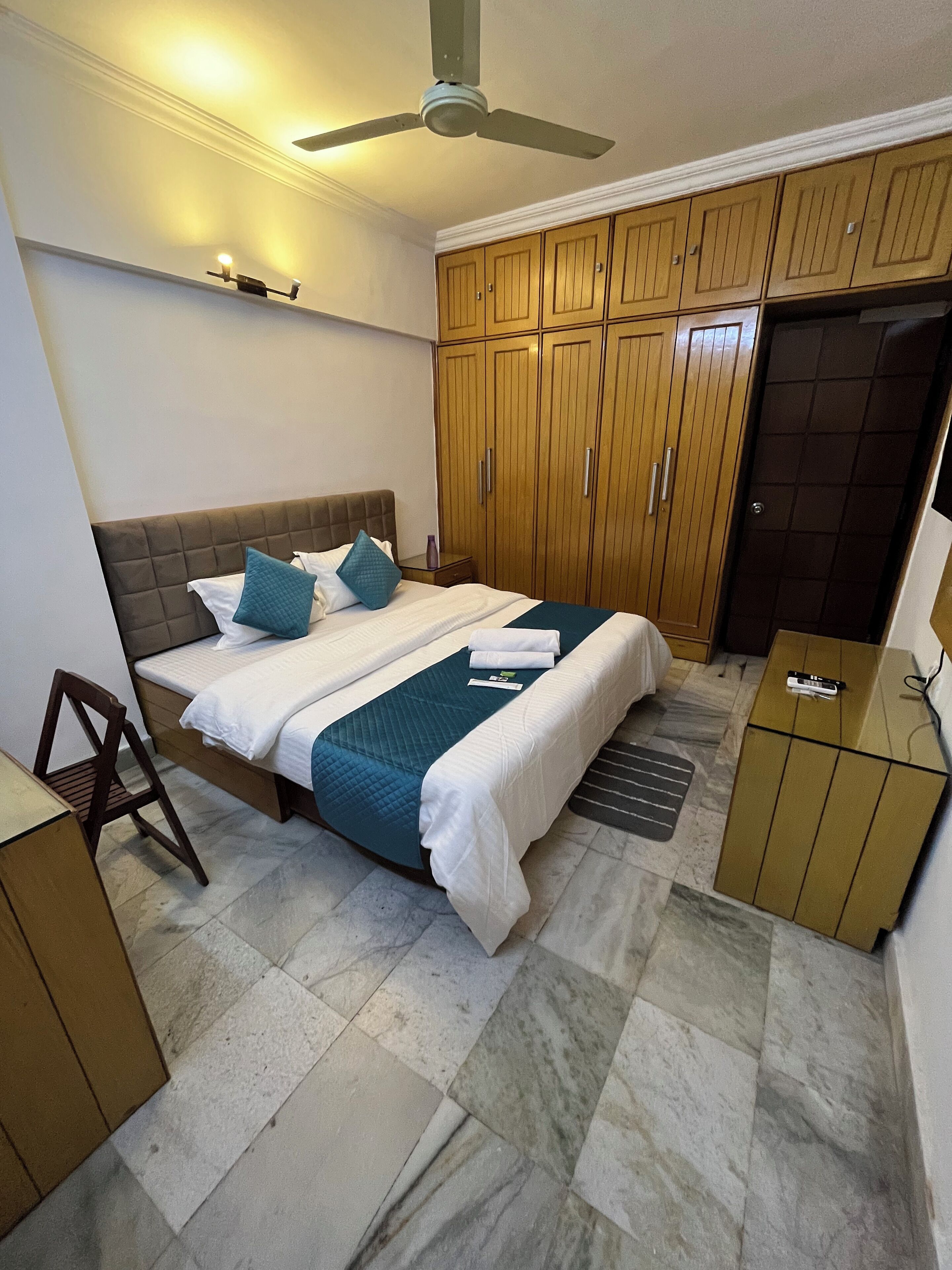 A bedroom with a bed, wooden wardrobe, bedside table, and a ceiling fan.