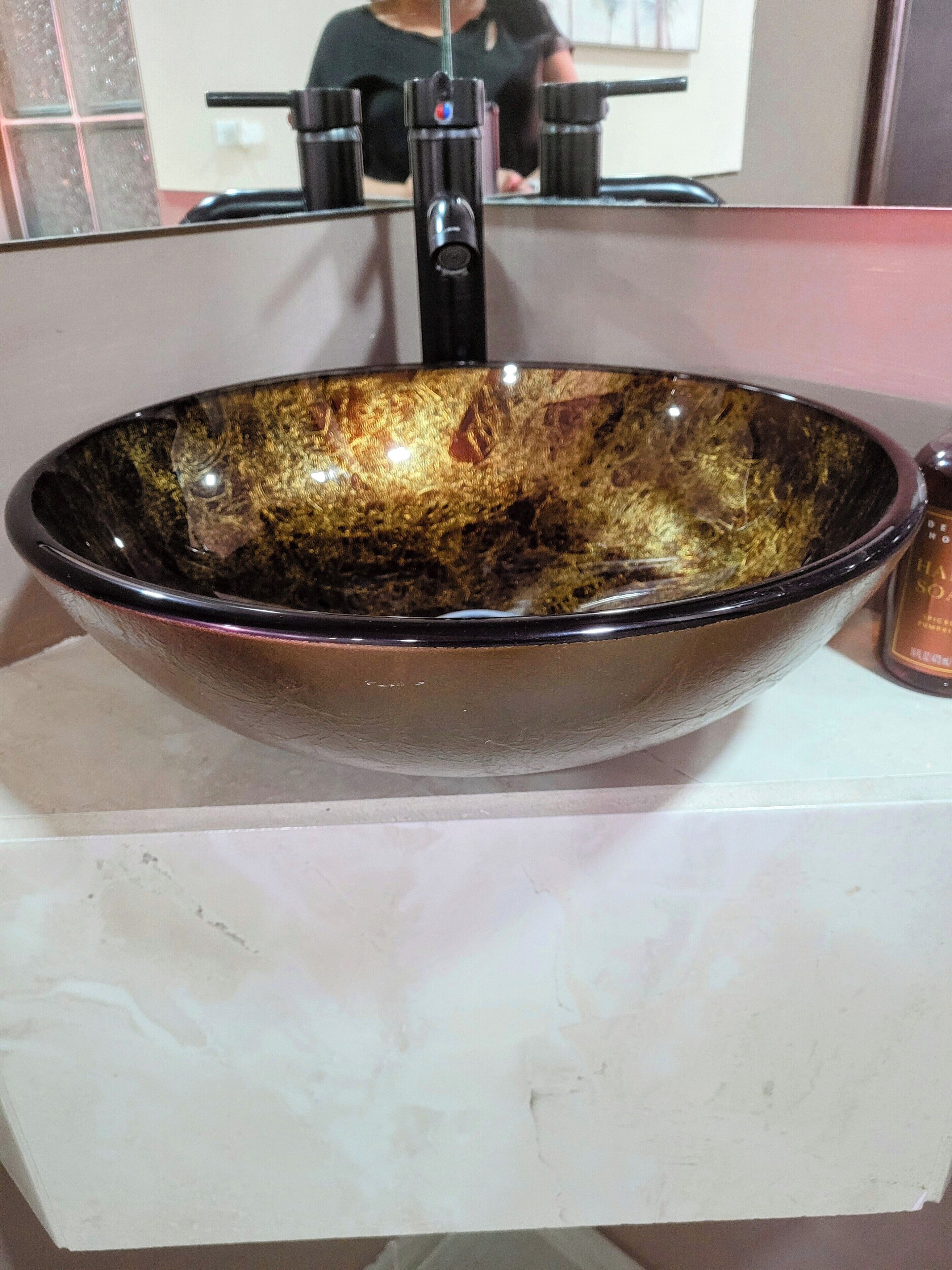 A large, oval-shaped vessel sink with a reflective, metallic finish, placed on a white marble countertop.