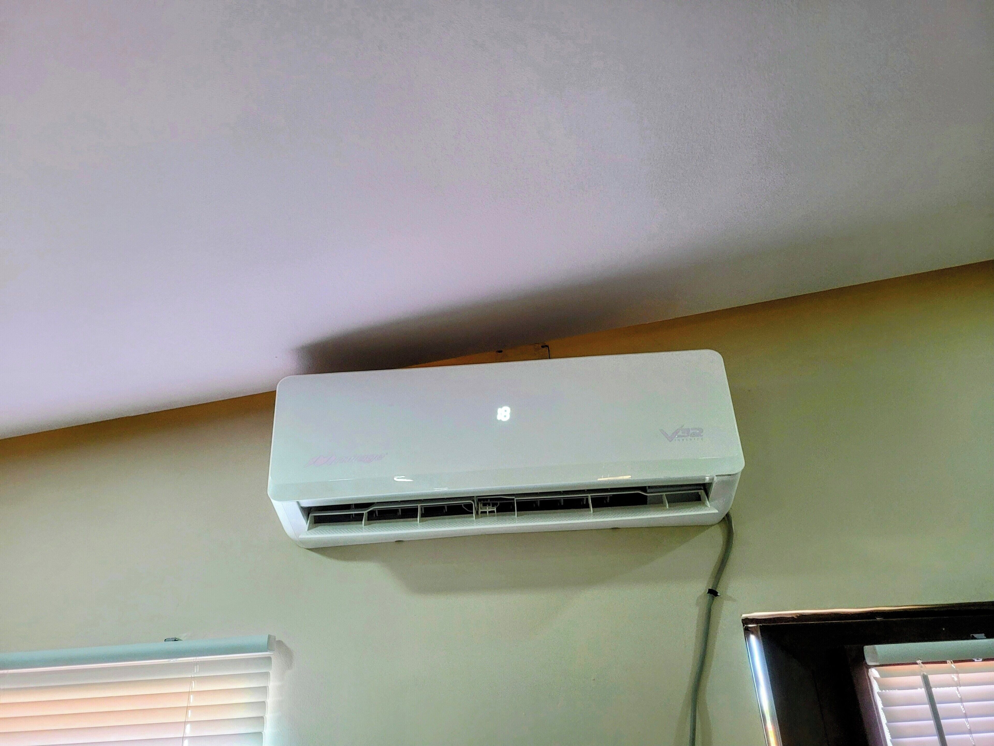 Un appareil de climatisation blanc, fixé au mur, avec une fenêtre en dessous.