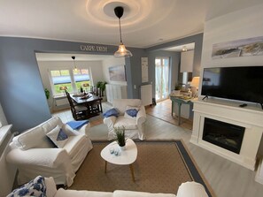 A living room with a fireplace, a television, and a dining area with a table and chairs. - Apartment 'Ferienwohnung Parkblick 1' with Private Terrace, Private Garden and Wi-Fi (Lübeck Travemünde)