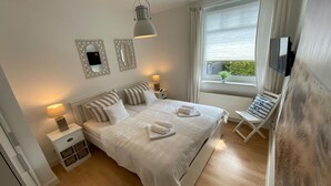 Quarto bem arrumado com cama, mesas de cabeceira, luminária, televisão e janela com vista.